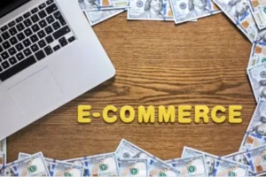A laptop surrounded by U.S. dollar bills, with the word 'Future of E-COMMERCE' spelled out in yellow letters on a wooden surface.