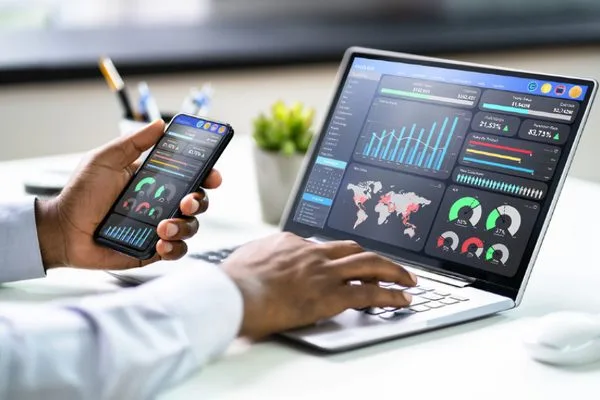 A person using a laptop and smartphone to monitor Social Media Analytics, featuring various graphs and charts on the laptop screen that display data insights and performance metrics.